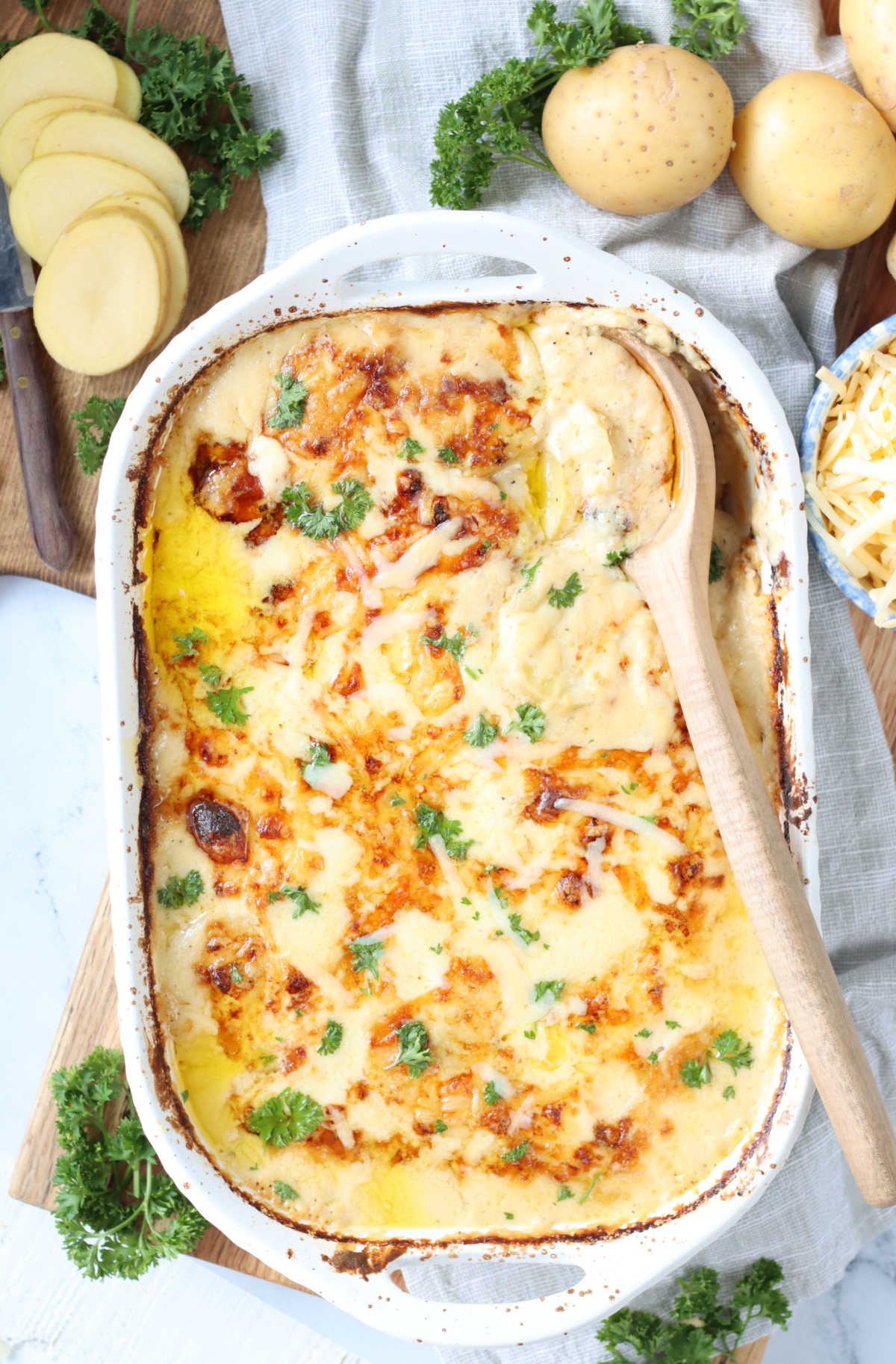Scalloped potatoes in white baking dish, slices of potatoes to the side.