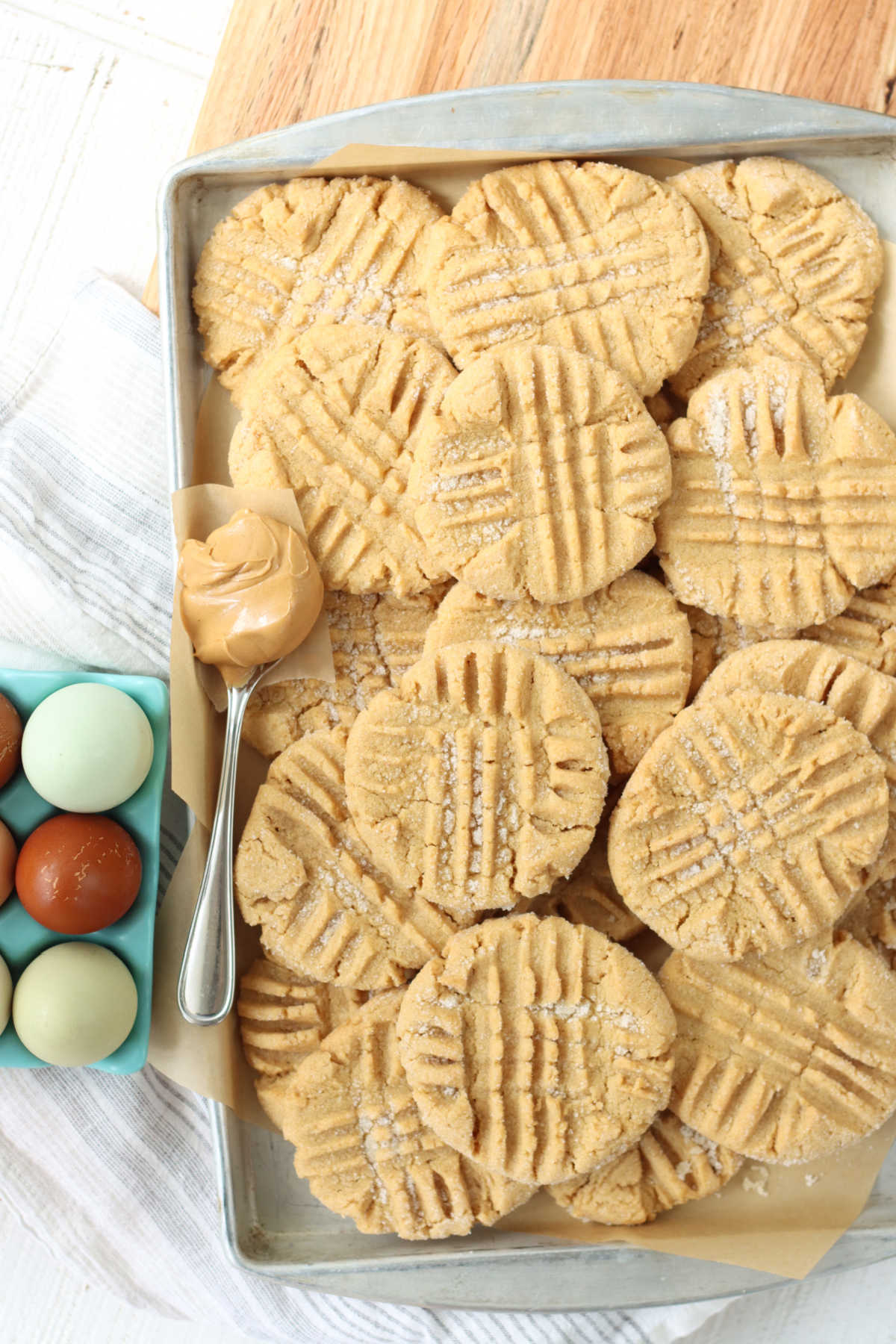 Peanut butter cookies stacked on metal sheet pan, spoon with scoop of peanut butter.