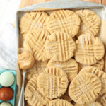 Peanut butter cookies on sheet pan, spoon with scoop of peanut butter.