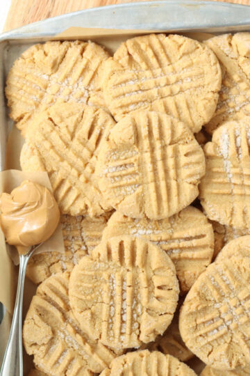Peanut butter cookies on sheet pan, spoon with scoop of peanut butter.