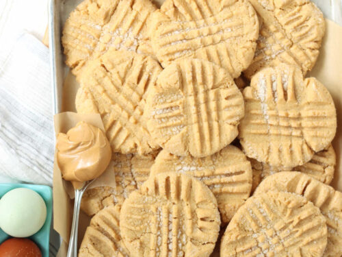 Peanut butter cookies on sheet pan, spoon with scoop of peanut butter.
