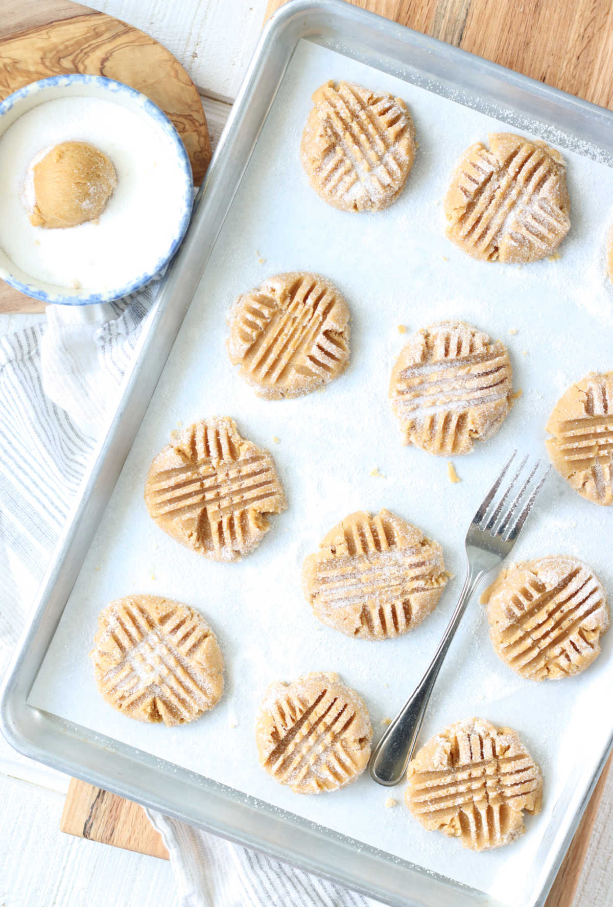 Pressing fork marks into peanut butter cookie dough on half sheet pan.