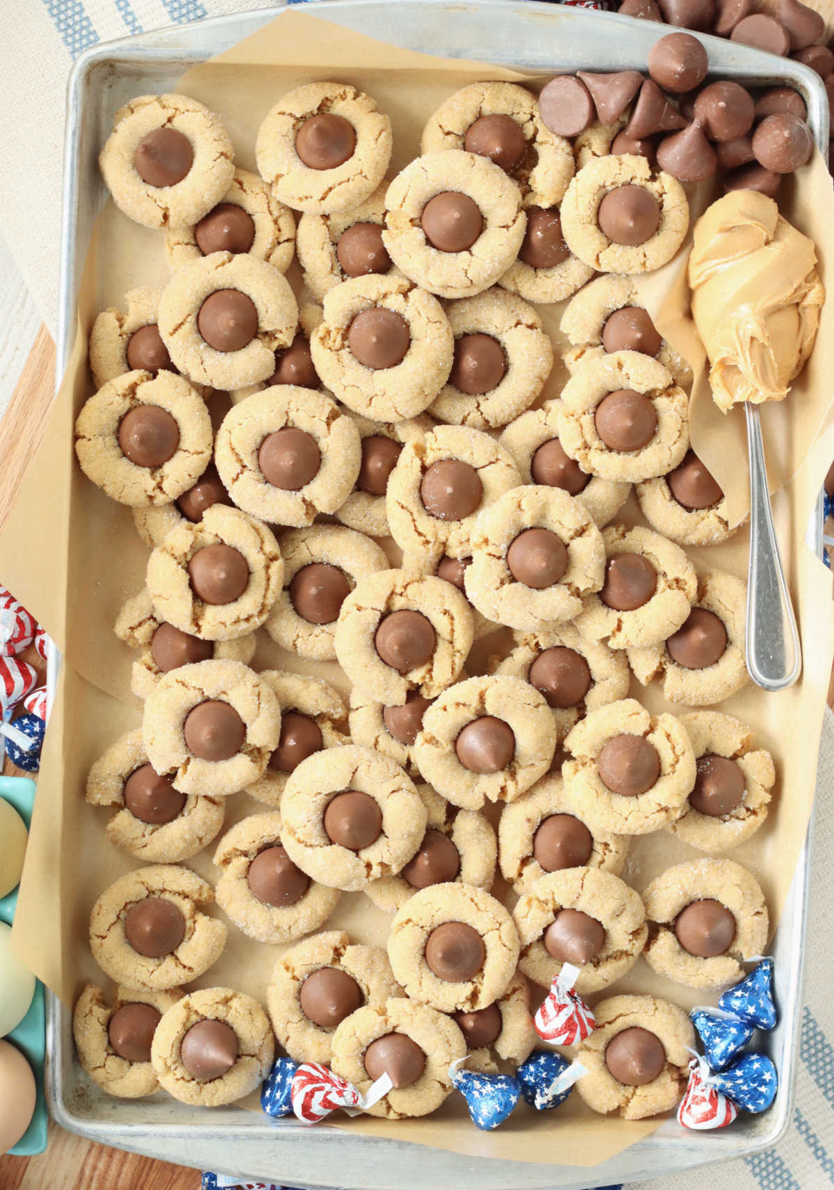 Peanut butter cookies with chocolate kisses on sheet pan, spoon heaping with peanut butter.