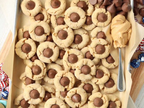 Peanut butter blossom cookies on sheet pan with spoonful of peanut butter and Hershey kisses.