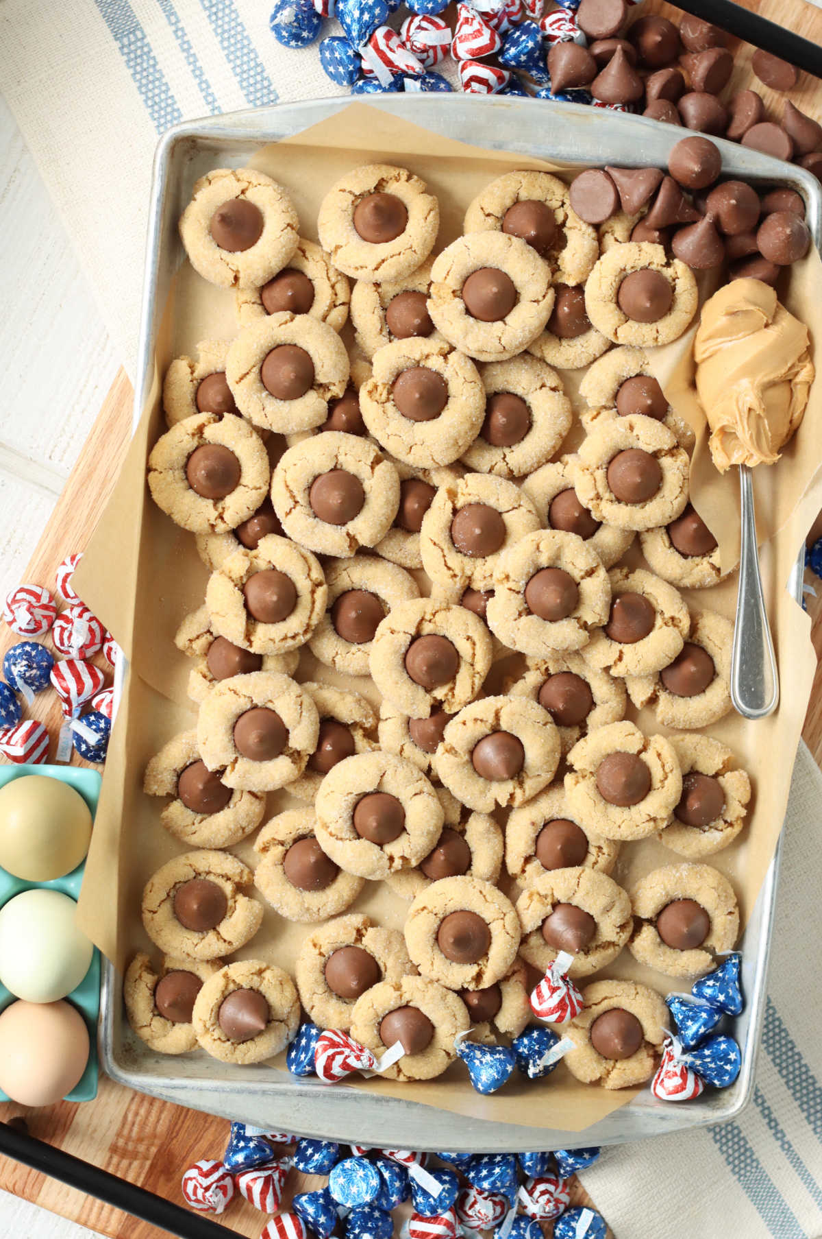 Sheet pan of peanut butter blossom cookies, spoonful of peanut butter on side.