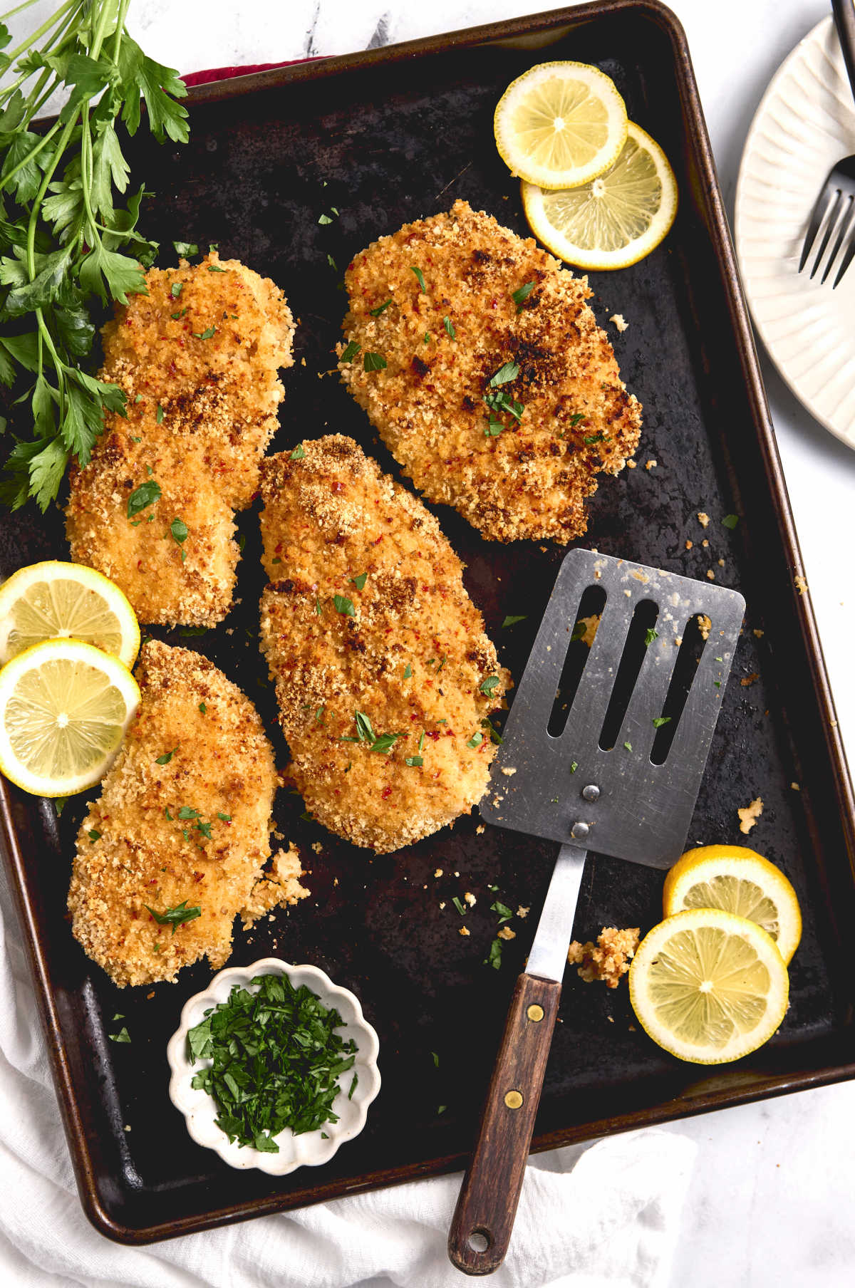 Breaded chicken breasts on sheet pan with parsley and lemon slices.