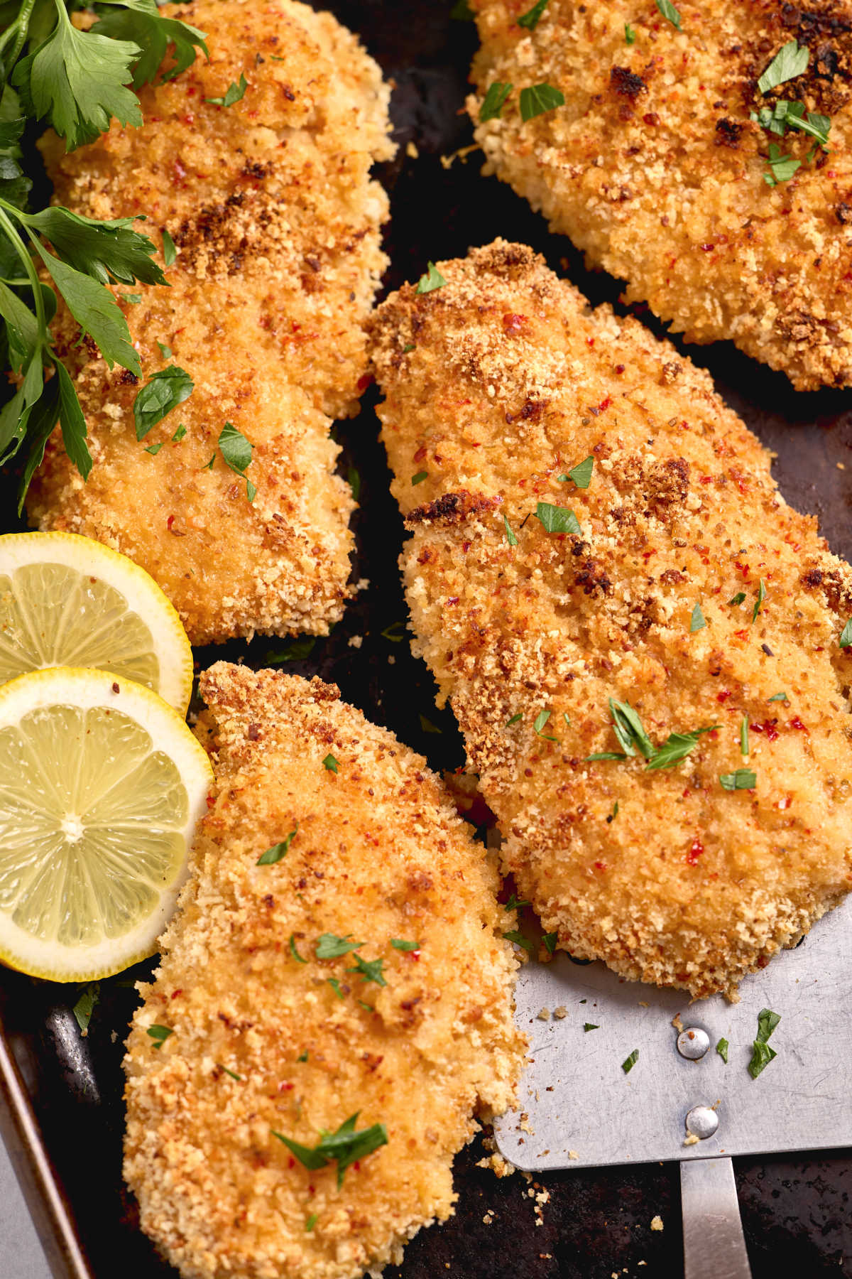 Breaded chicken on sheet pan, fresh parsley and lemon slices.
