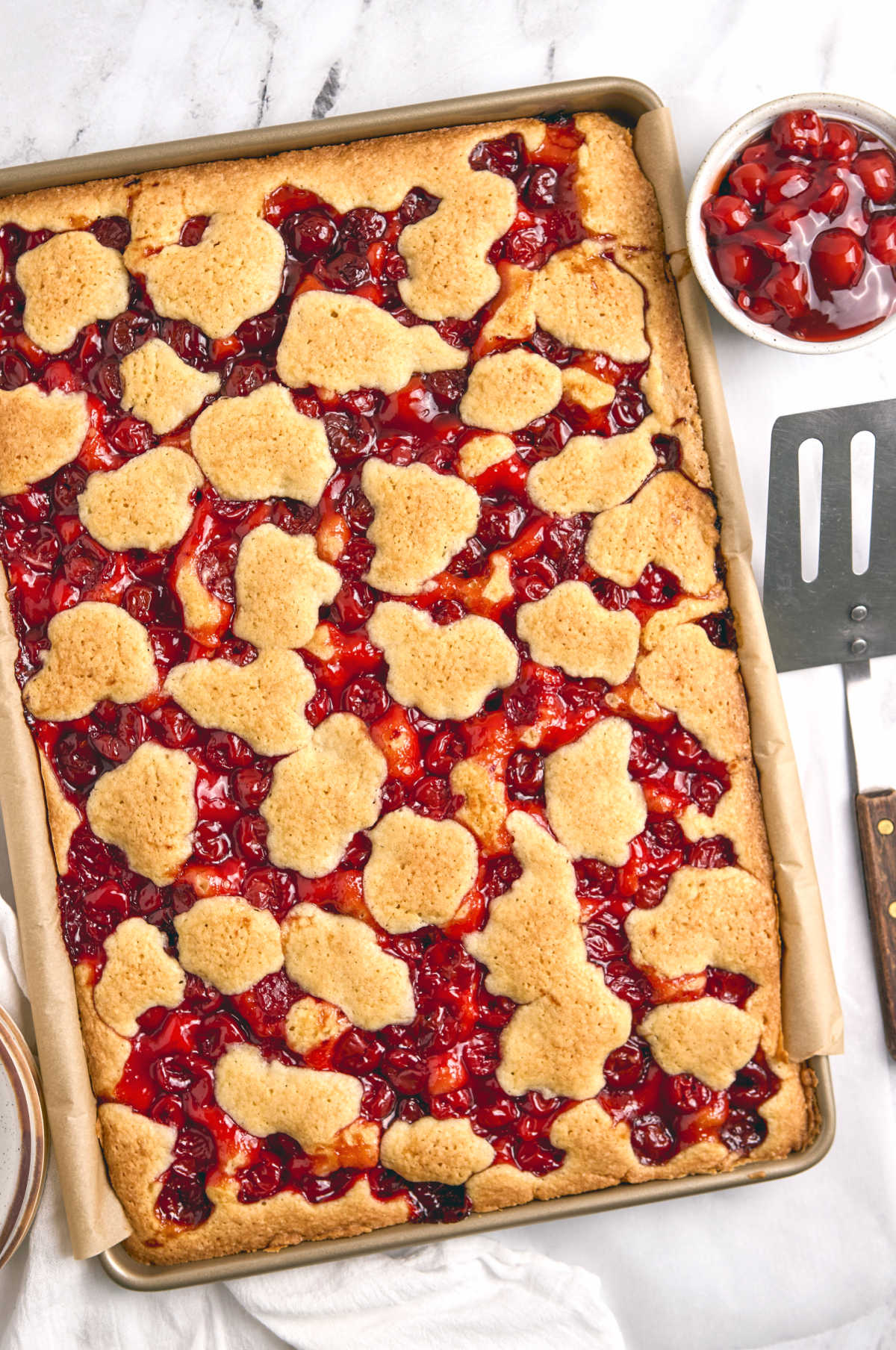Cherry pie bars in metal baking pan with spatula.