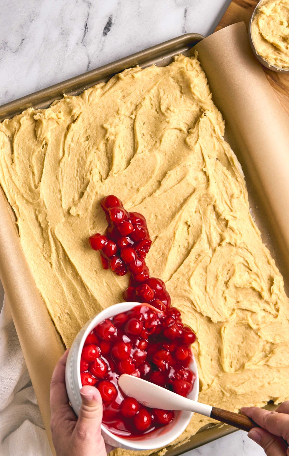 Pouring cherry filling onto bottom crust in sheet pan.