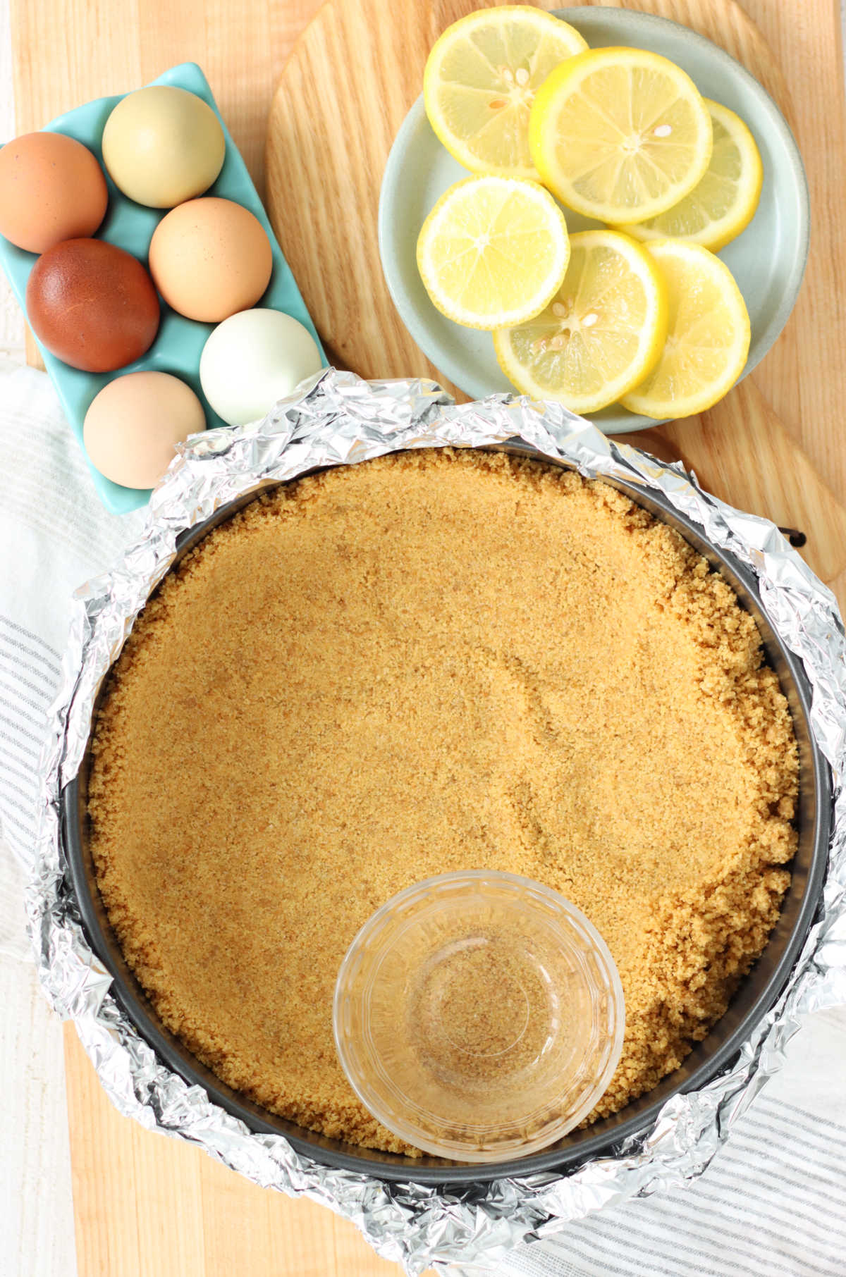 Pressing graham cracker crust in springform pan with small round glass.