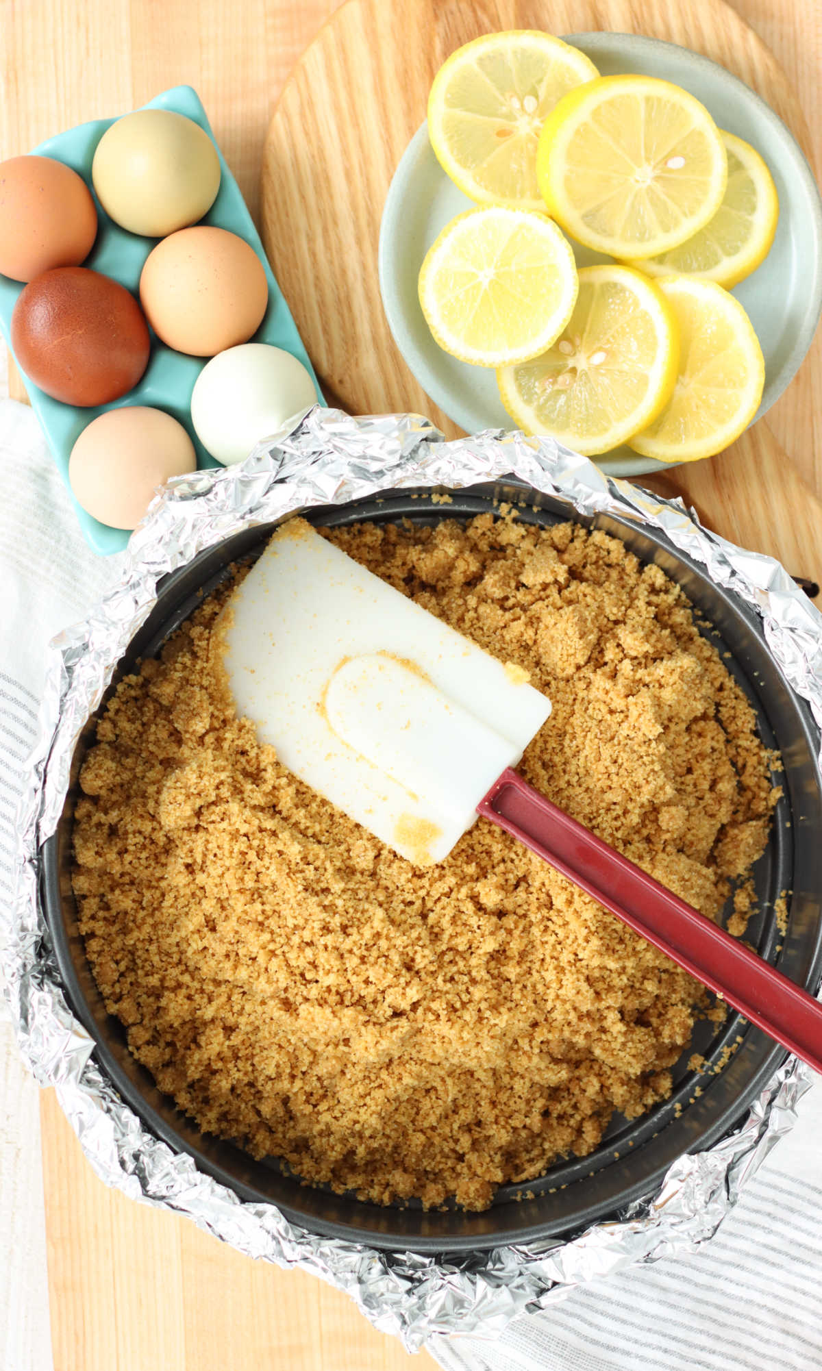 Filling springform pan with graham cracker crust, red handle spatula in pan.