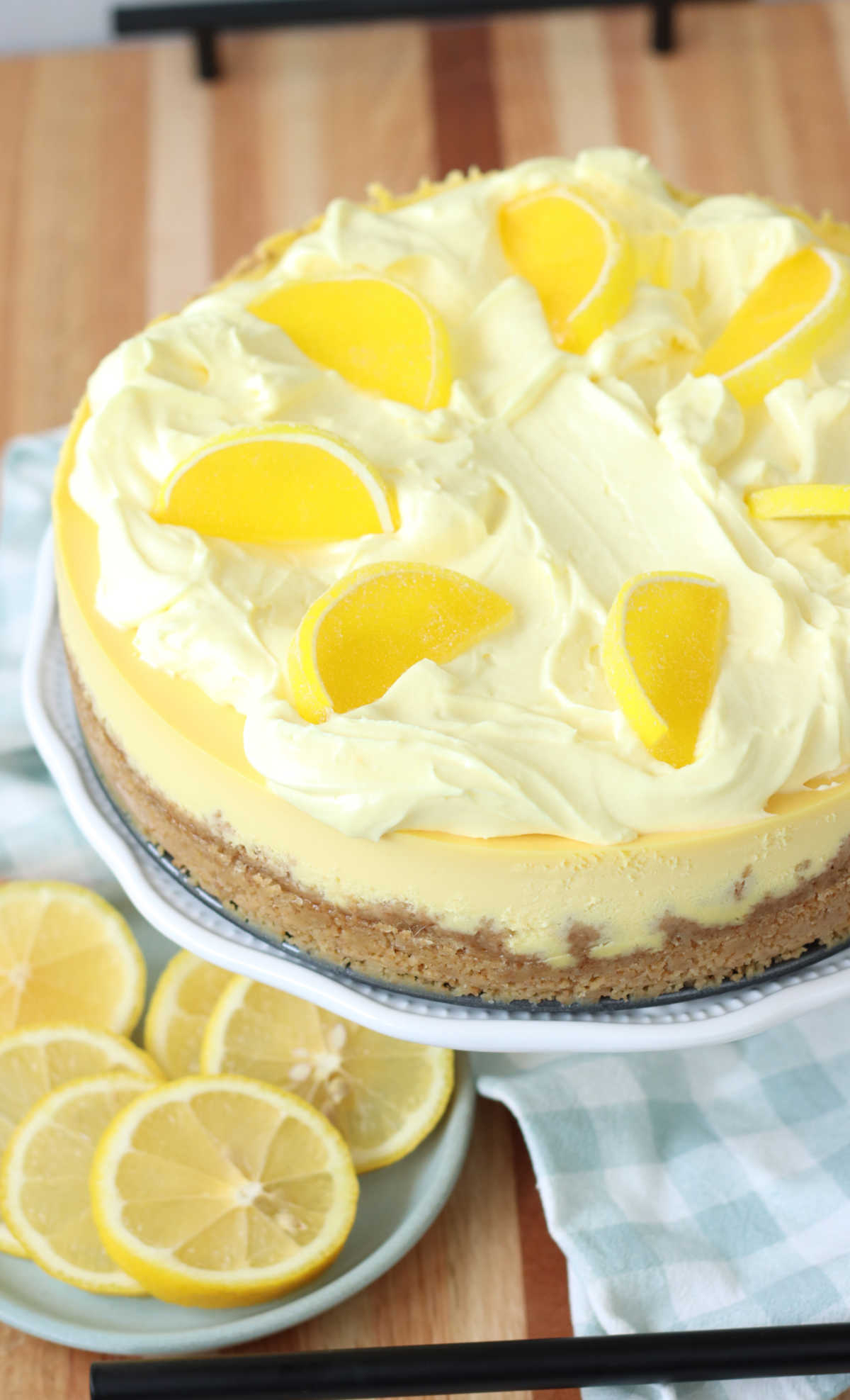 Lemon cheesecake on white footed cake dish topped with Boston fruit slices.
