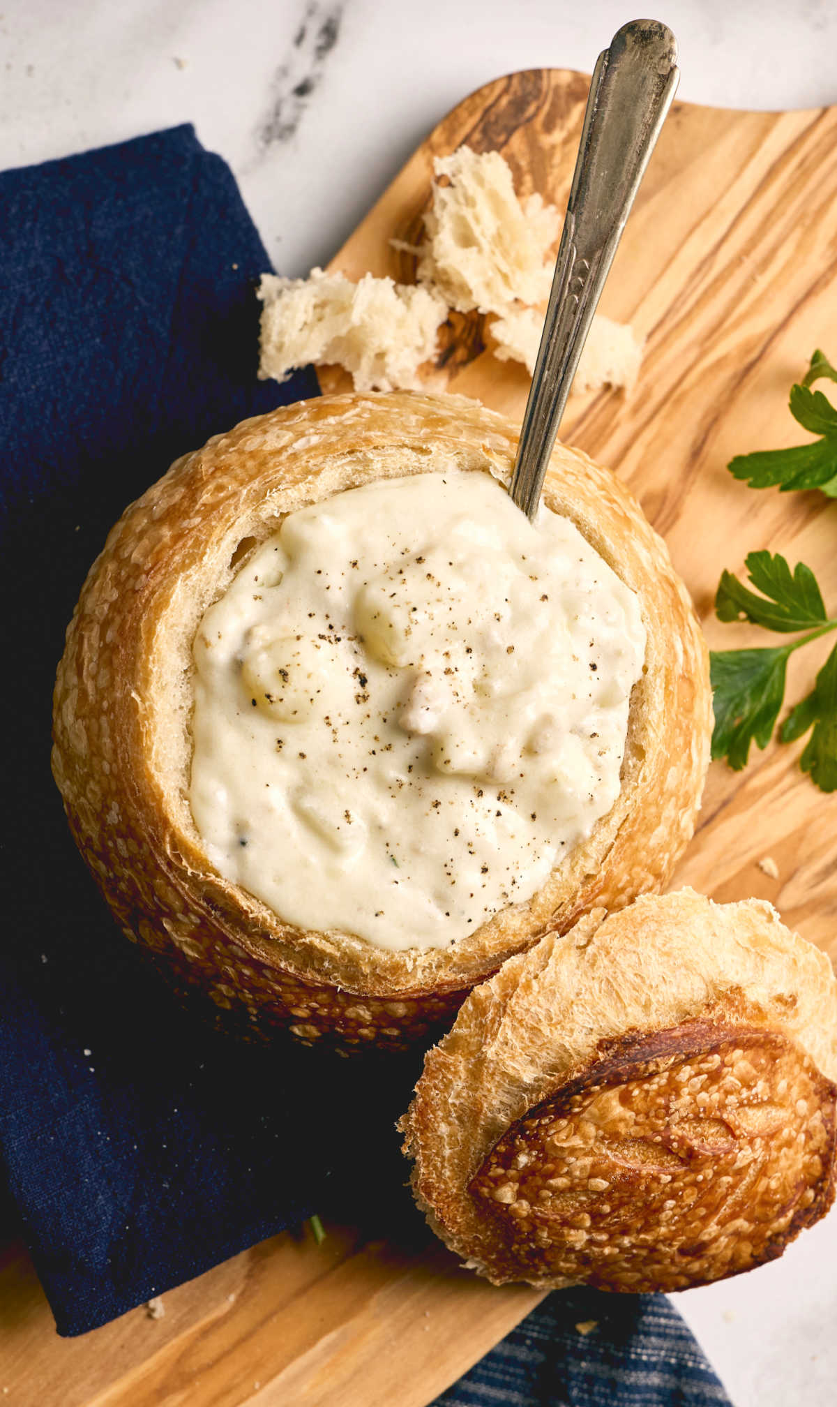 Clam chowder in bread bowl on wooden cutting board.