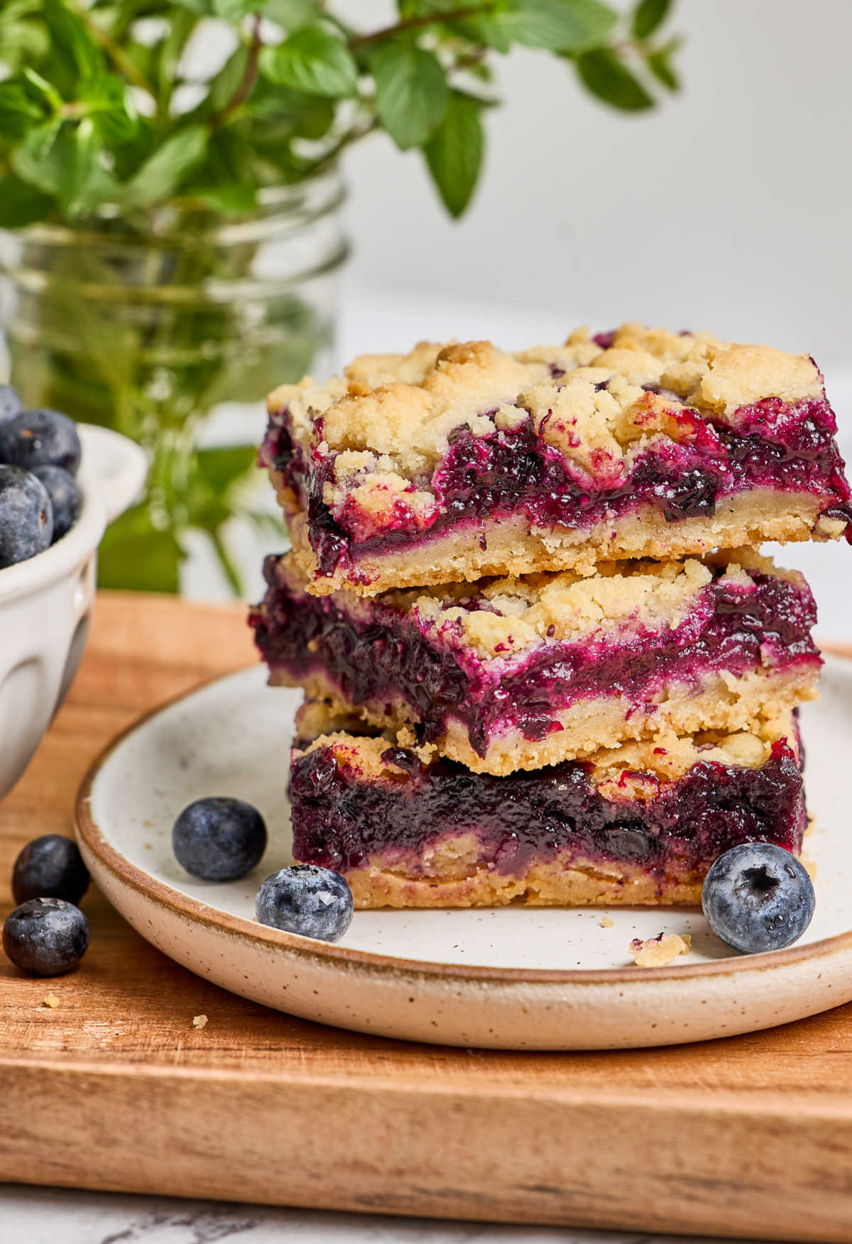Blueberry bars stacked on small white speckled plate, fresh blueberries around.