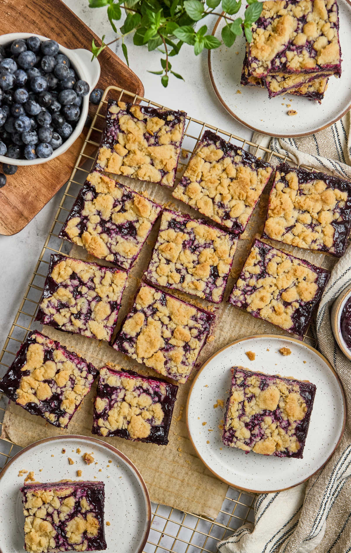 Blueberry crumb bars cut into squares on metal rack, one on small white speckled plate.