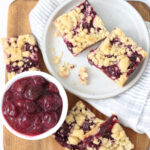 Cherry bar squares on small plate on wooden cutting board.
