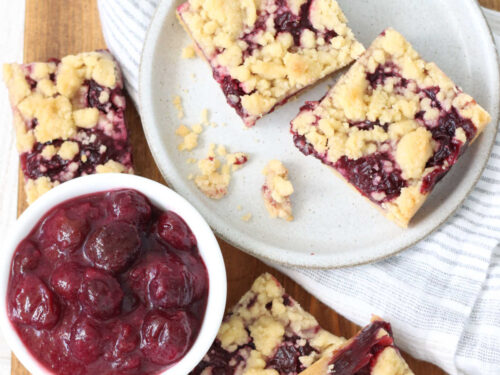 Cherry bar squares on small plate on wooden cutting board.