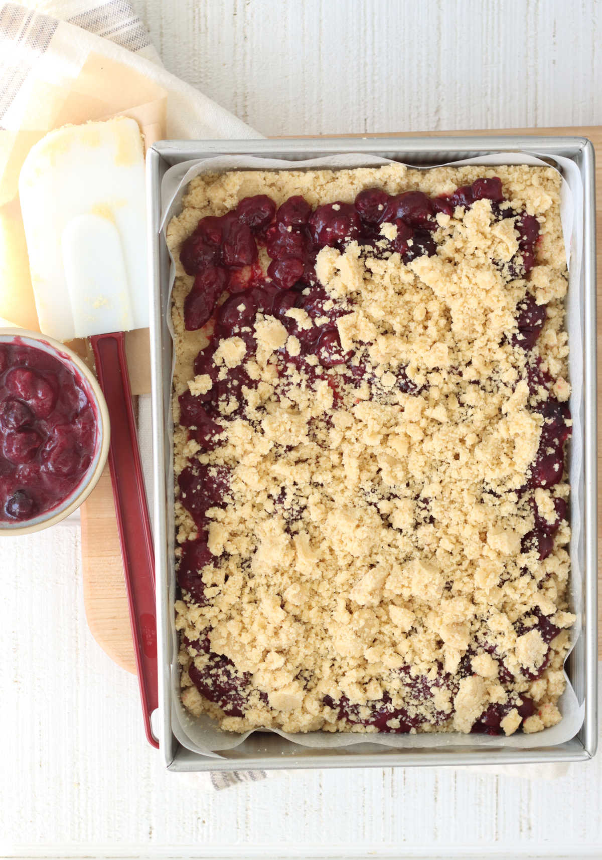 Putting crumb topping on cherry bars in 9x13-inch baking pan, rubber spatula to left.