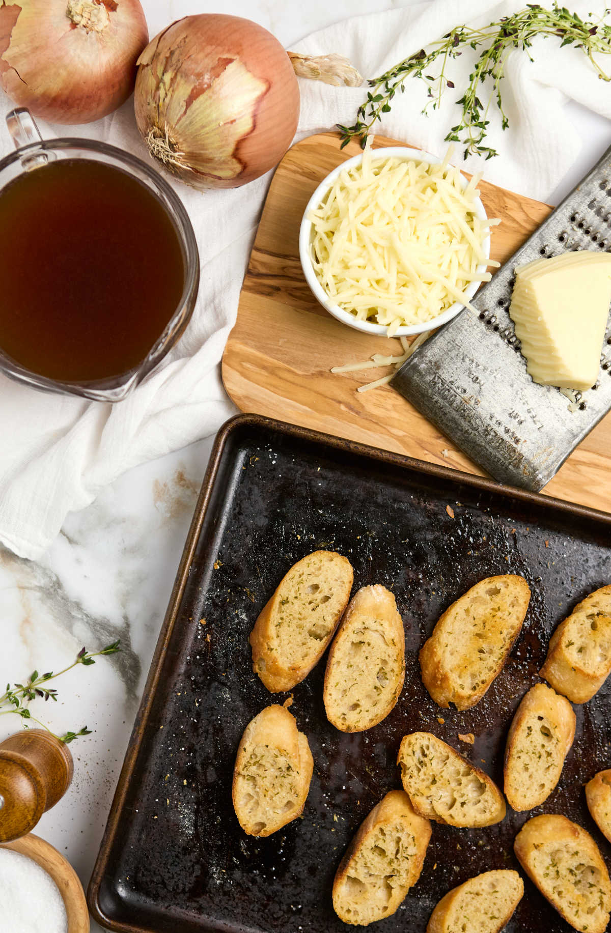 Baguette slices on sheet pan, ingredients for onion soup.