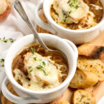 French onion soup in white crocks on wood cutting board.
