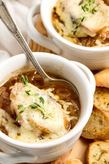 French onion soup in white crocks on wood cutting board.
