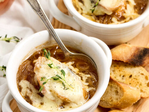 French onion soup in white crocks on wood cutting board.