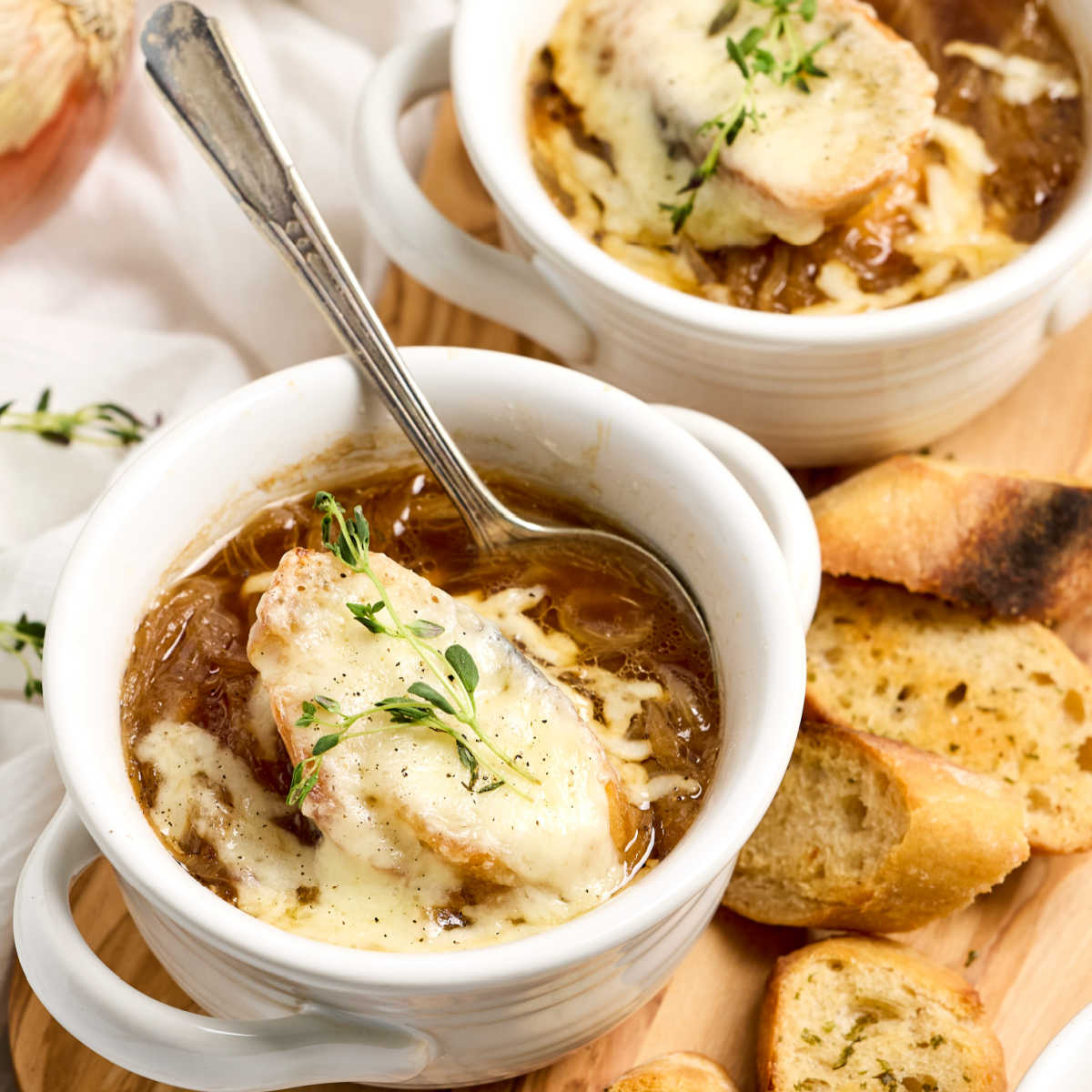 French onion soup in white crocks on wood cutting board.