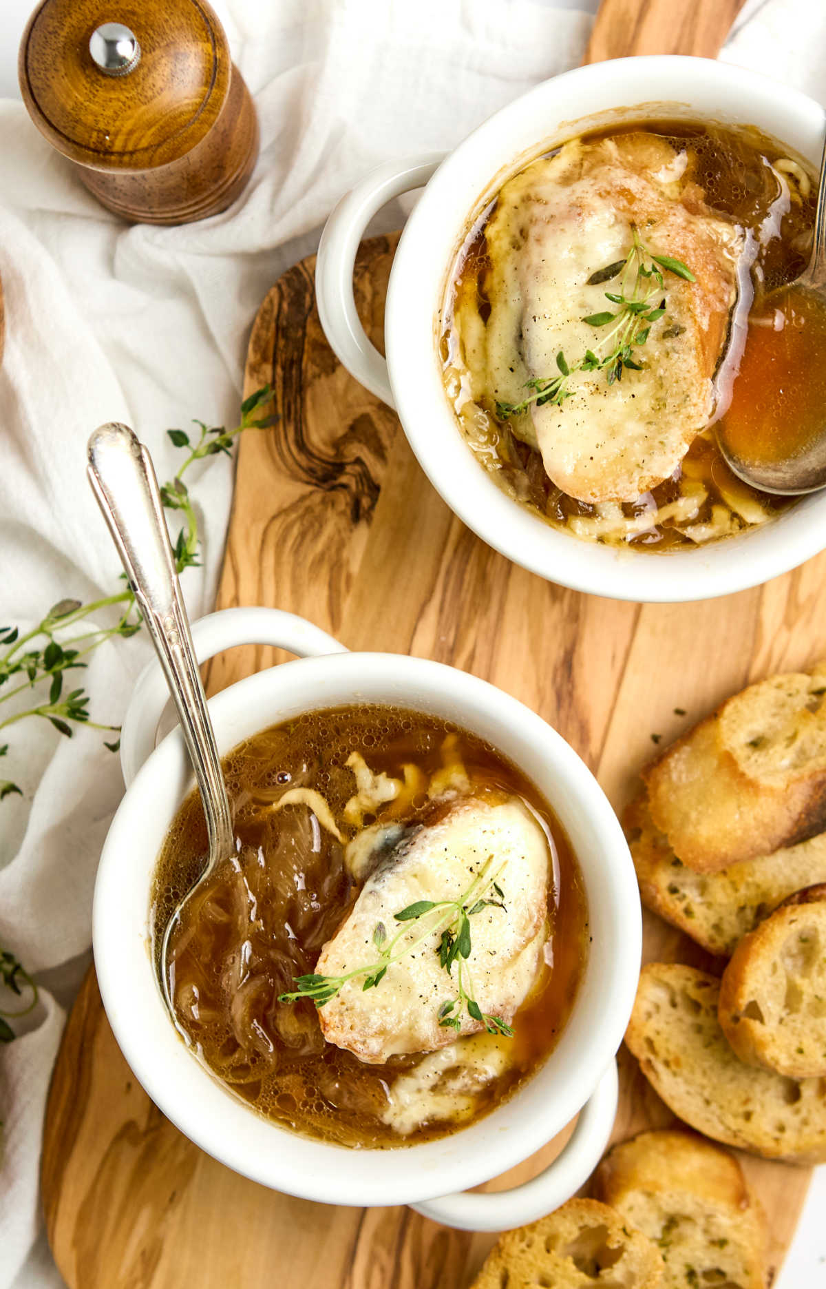 Soup crocks with onion soup, baguettes and melted cheese on wooden cutting board.