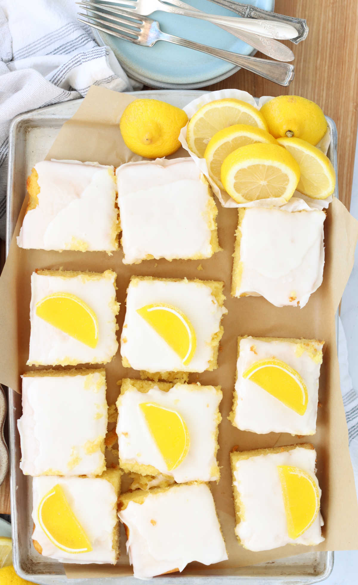 Squares of lemon cake on sheet pan, lemon slices to side.