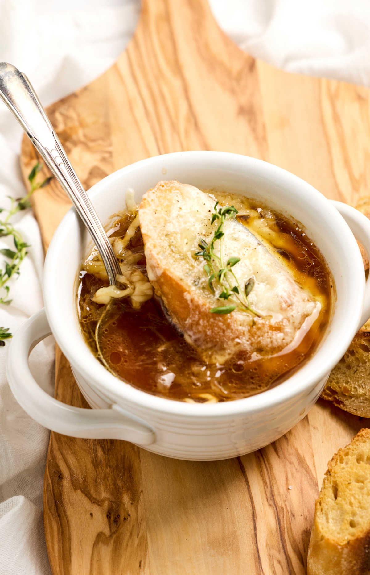 Onion soup, baguette and melted cheese, topped with fresh thyme in white soup crock.