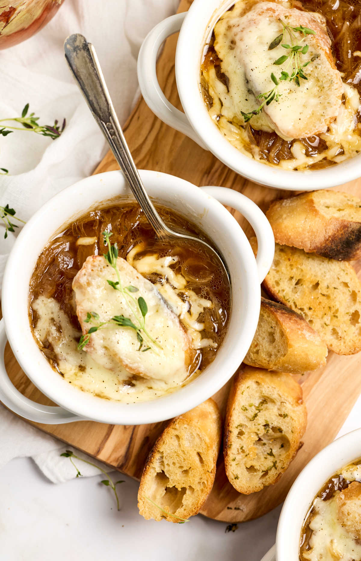 French onion soup in white crock, topped with baguette and melted cheese.