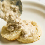 Spooning sausage gravy over biscuit on plate.