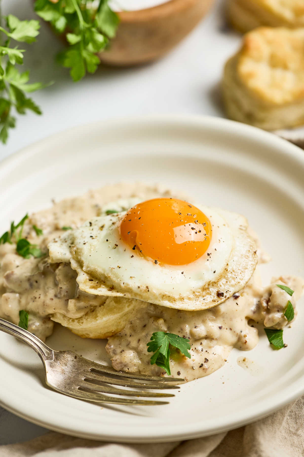 Fried egg on top of biscuits and gravy with fork on small white plate.