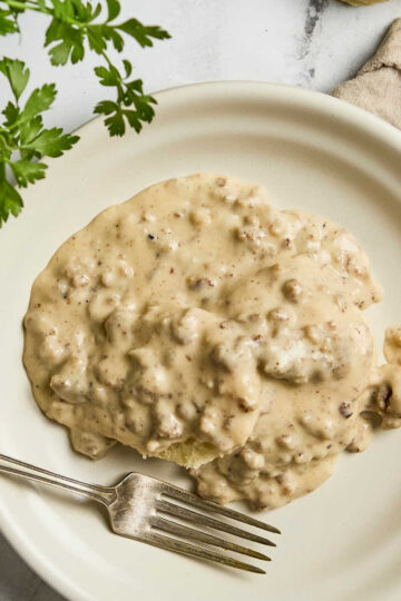 Biscuits and gravy on small white plate with fork.