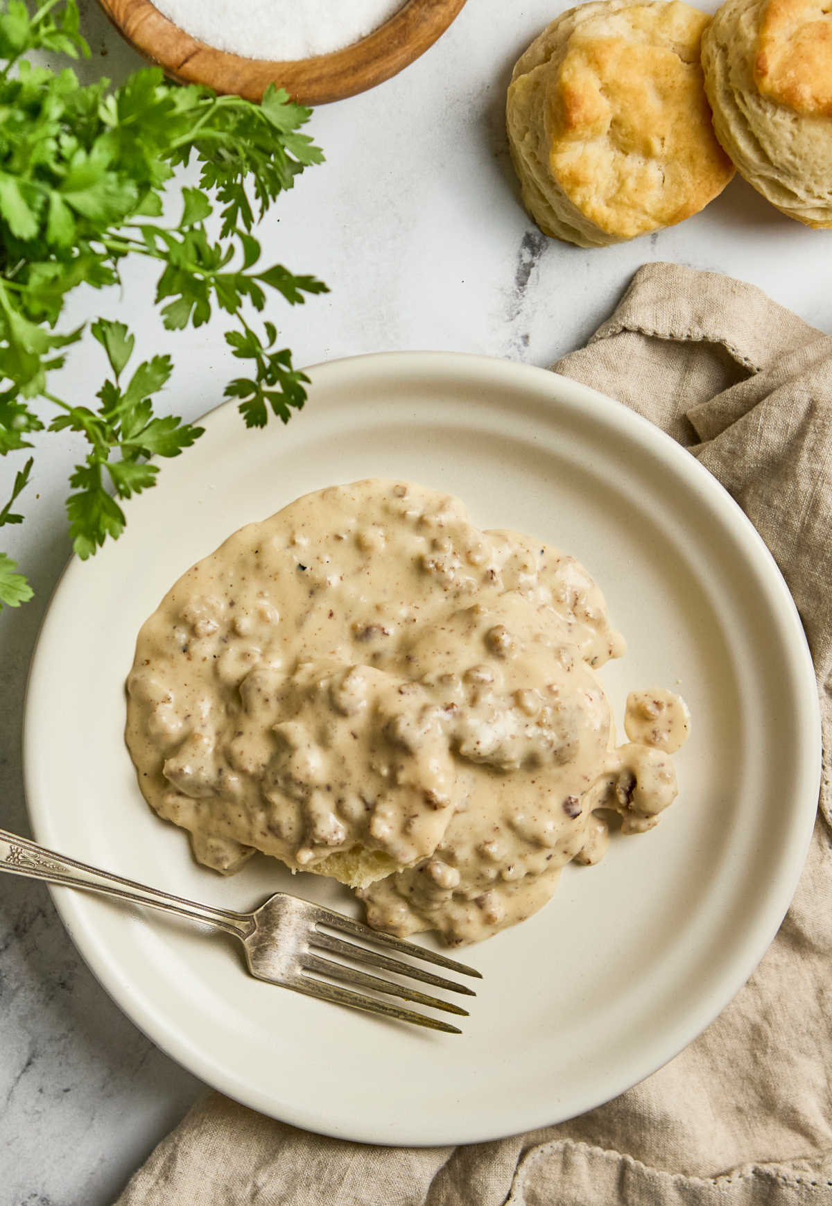 Sausage gravy over biscuits on small white plate.