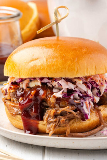 BBQ pork sandwich with coleslaw on small plate, pickles in small bowl.