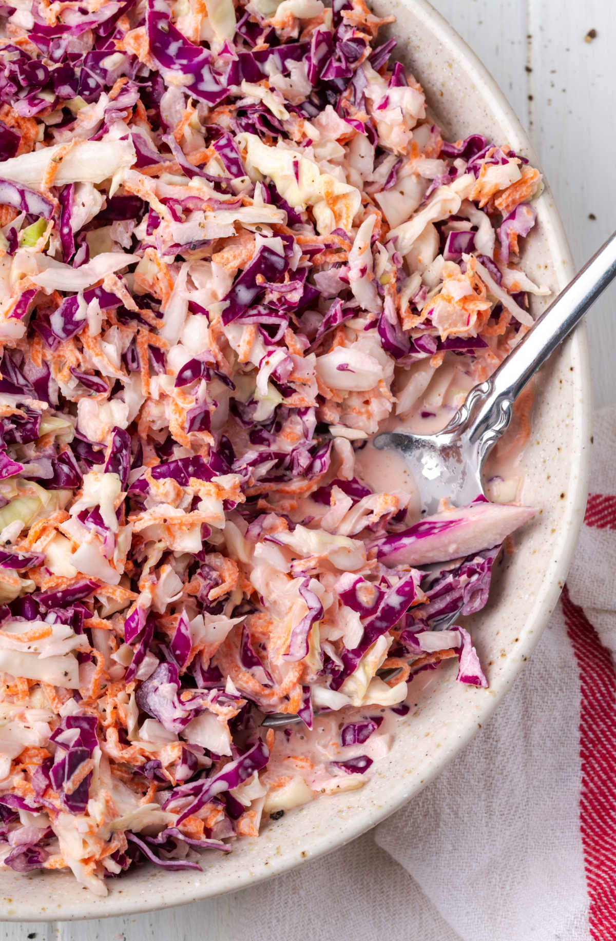 Closeup of coleslaw in white speckled bowl with serving spoon.