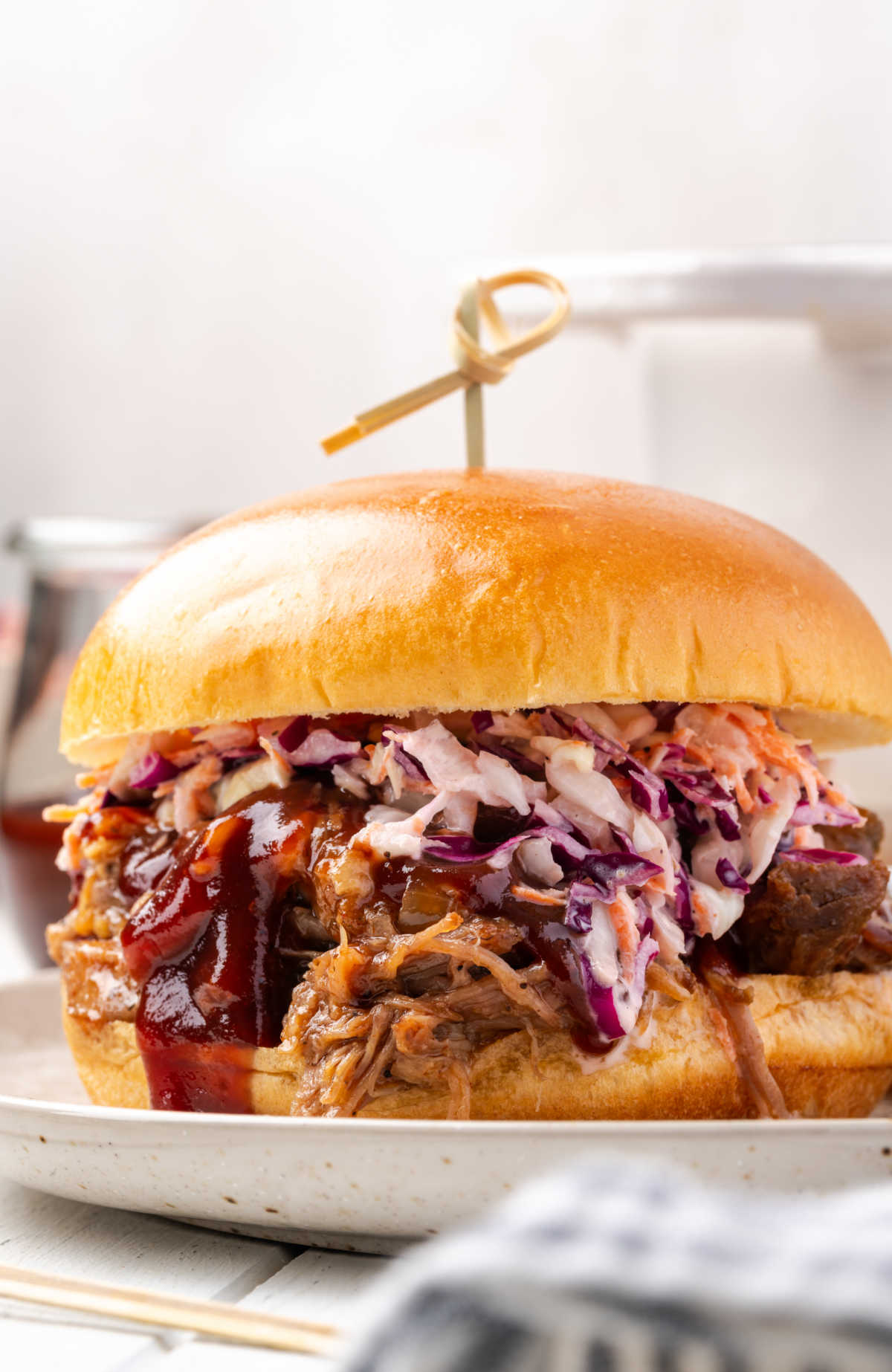 BBQ pork sandwich with coleslaw and pickles on small plate.