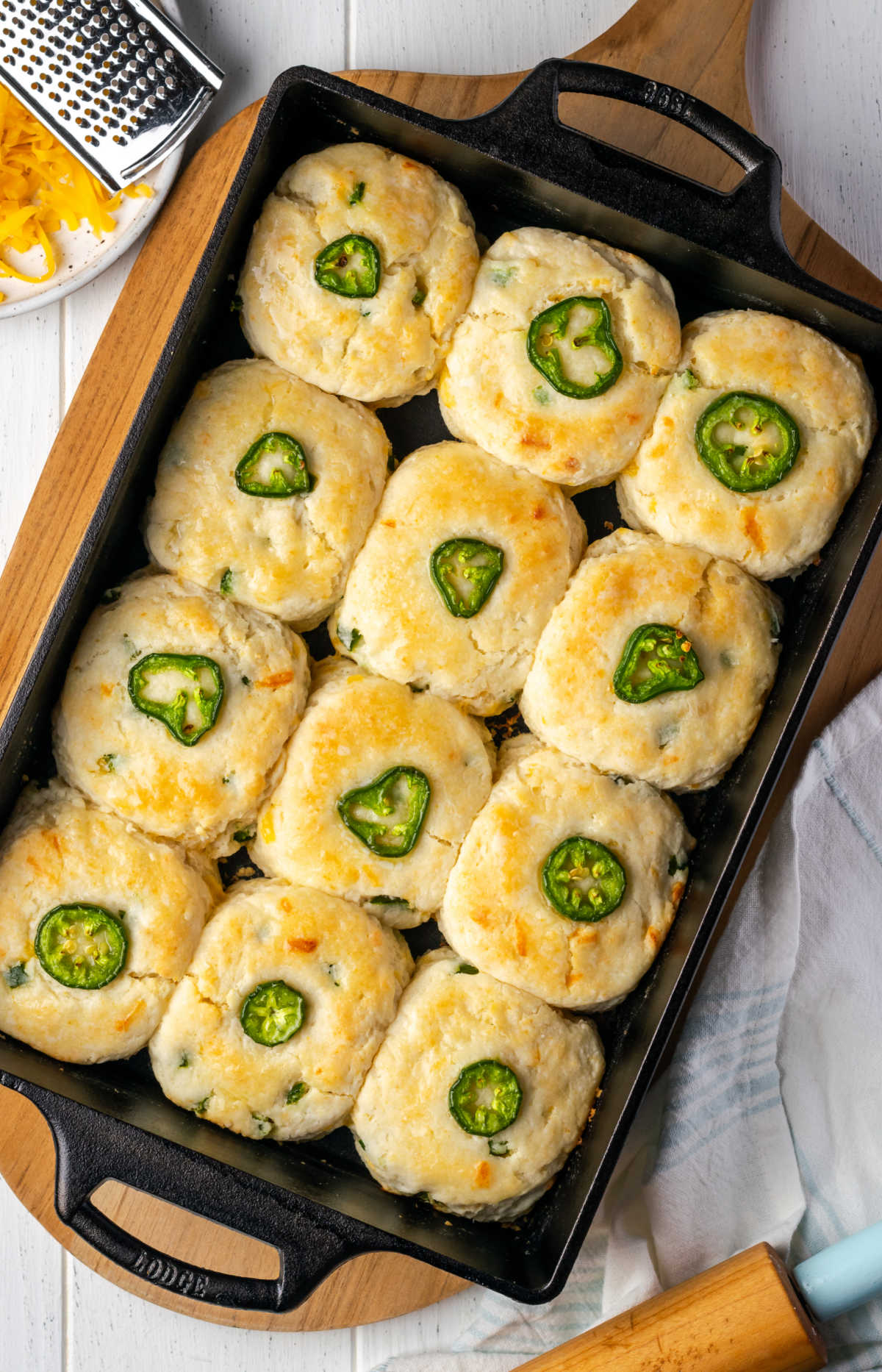 Baked jalapeno cheddar biscuits with jalapeno slices on top of biscuits in rectangle cast iron baking pan.