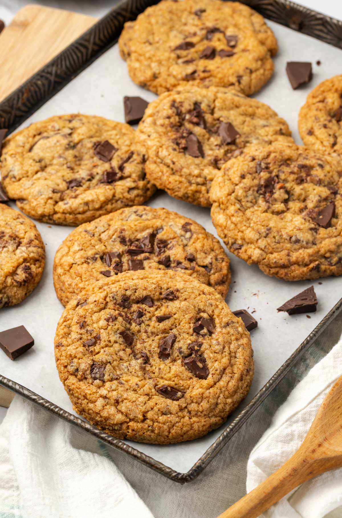 Chocolate chunk cookies piled on half sheet pan, pieces of chocolate around.