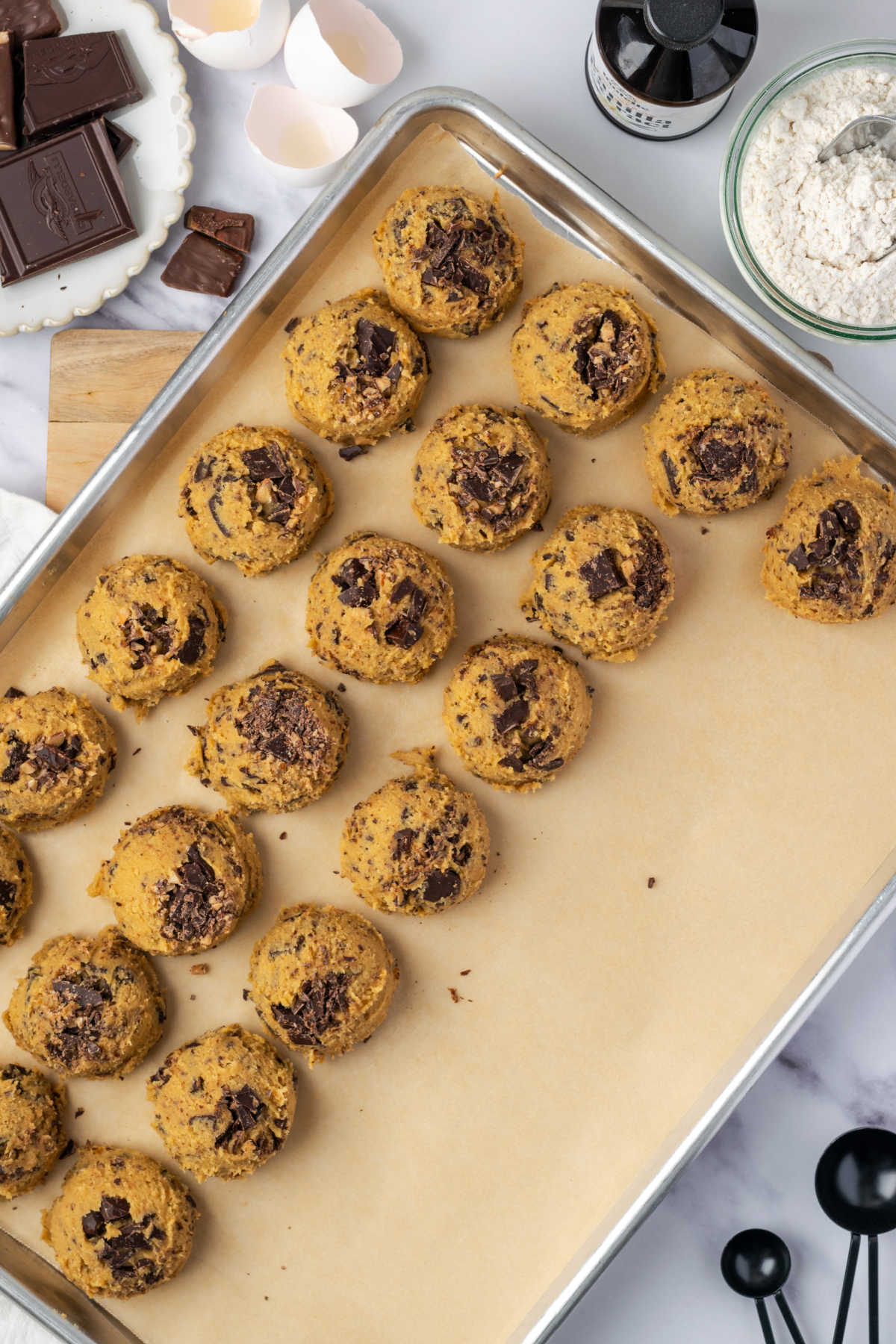 Scooped cookie rounds on half sheet pan with brown parchment paper.
