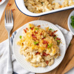 Baked mac and cheese, breadcrumb topping, bacon, green onion on small white plate with fork.