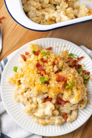 Baked mac and cheese, breadcrumb topping, bacon, green onion on small white plate with fork.