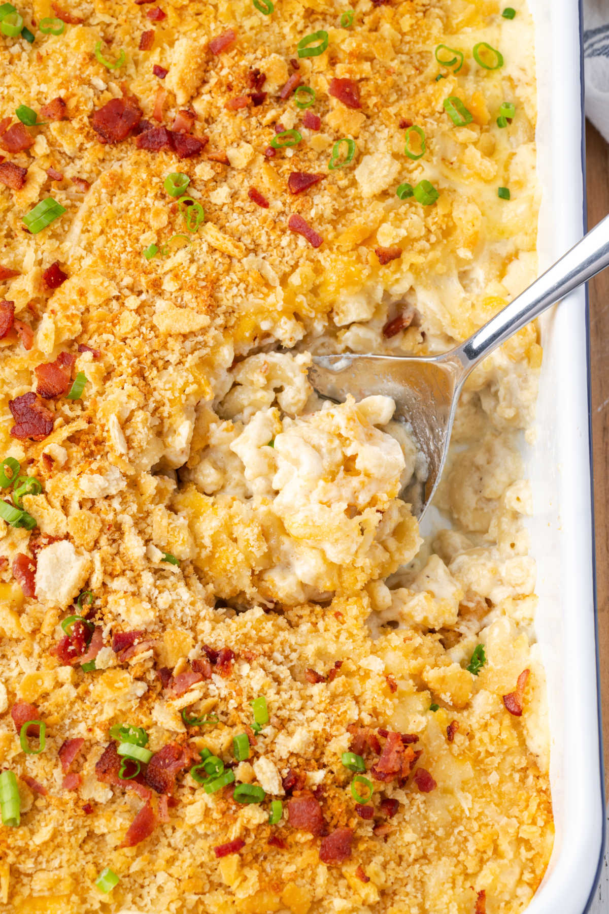 Spoon in white casserole dish of baked mac and cheese.