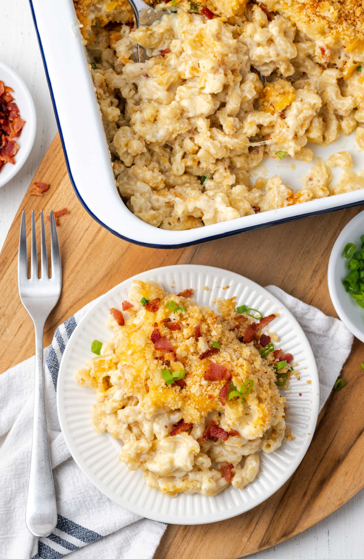 Mac and cheese with breadcrumb topping, bacon, green onion slices on small white plate with fork.