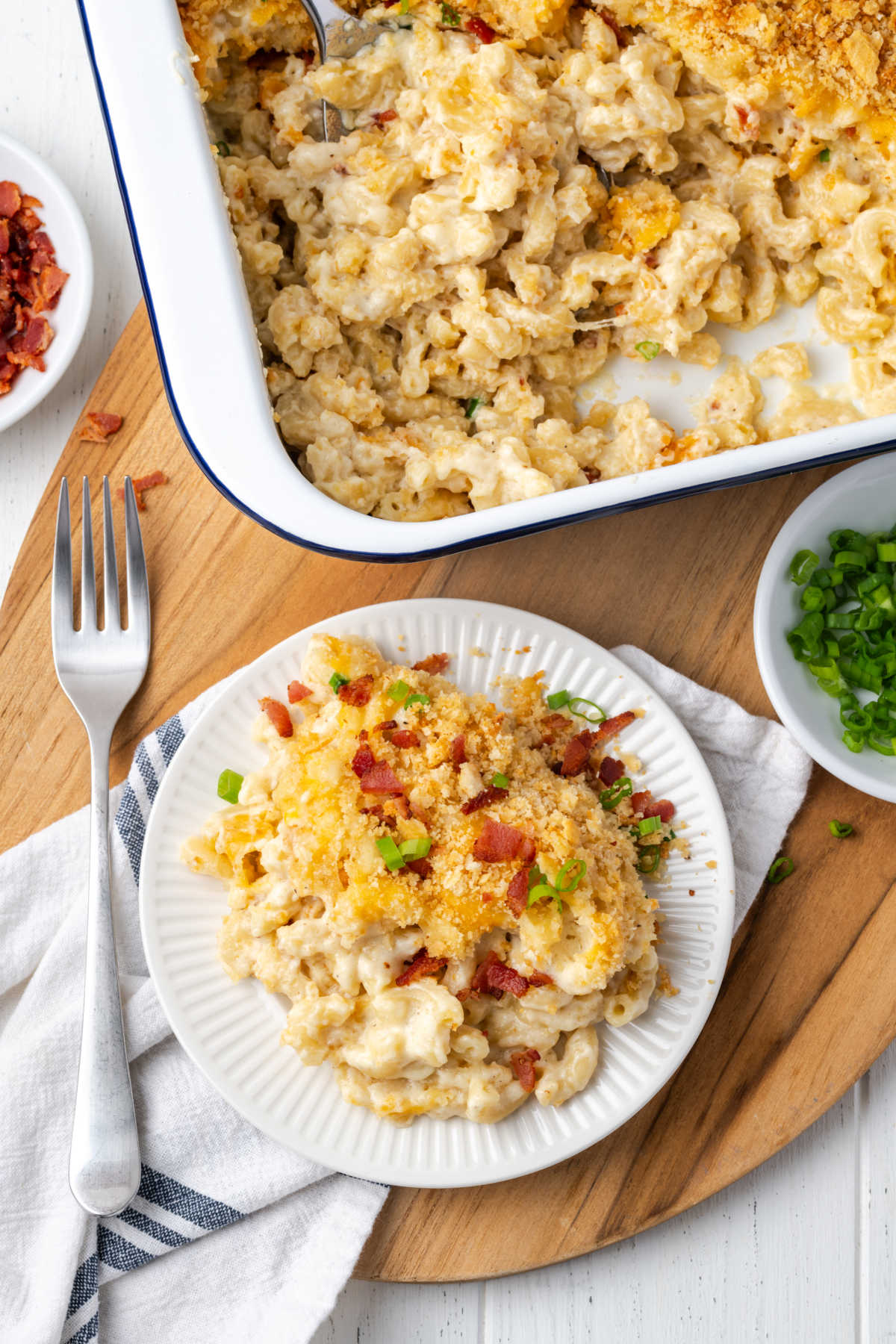 Mac and cheese with breadcrumb topping, bacon and green onion on small white plate with fork.
