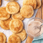 Snickerdoodles on white parchment, cinnamon sugar in clear glass bowl.