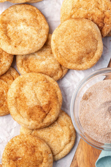 Snickerdoodles on white parchment, cinnamon sugar in clear glass bowl.