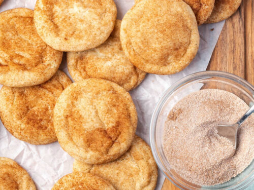 Snickerdoodles on white parchment, cinnamon sugar in clear glass bowl.