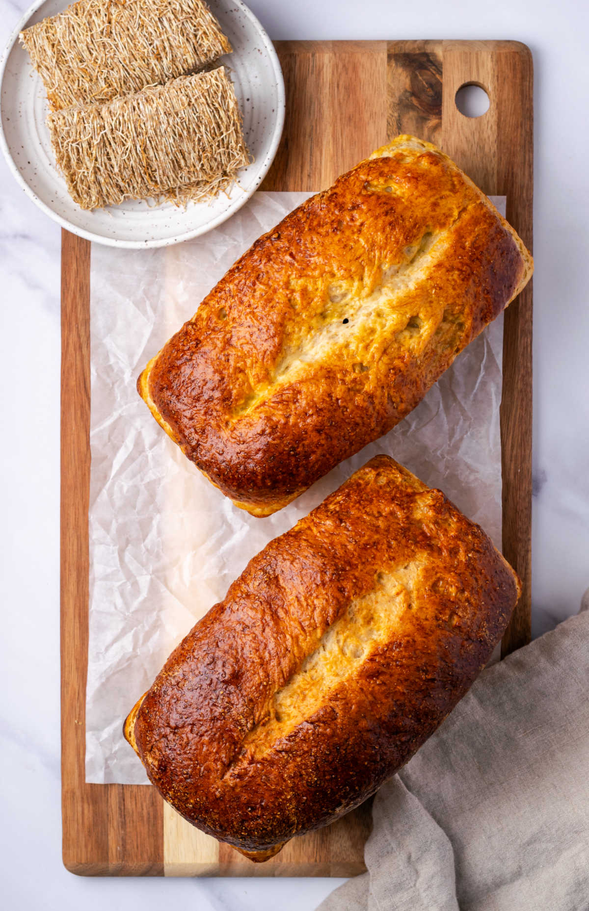 Shredded wheat bread on cutting board, biscuits on small speckled plate.